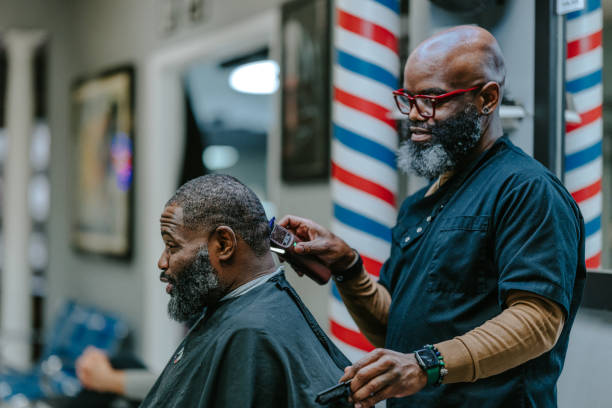 Profile view of a mature adult black man talking with his barber while having his hair trimmed.