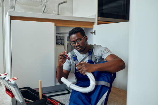 Black plumber in uniform fixing kitchen sink He is sitting on the floor in kitchen and holding pipe